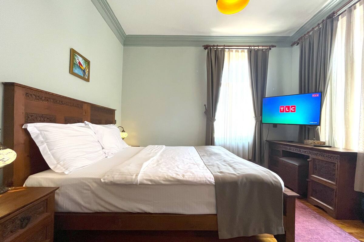 A hotel room with a bed, a television, a desk, and a window with curtains.