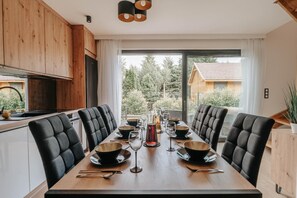 A modern dining area with a long table set for six, surrounded by black upholstered chairs. - Holiday Home Near the Sea, air Conditioning (Ustronie Morskie)