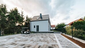 A modern building with a paved driveway, a parked golf cart, and a fenced garden area. - Holiday Home Near the Sea, air Conditioning (Ustronie Morskie)