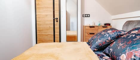 A bedroom with a bed, a wooden wardrobe, a dresser, and a mirror.