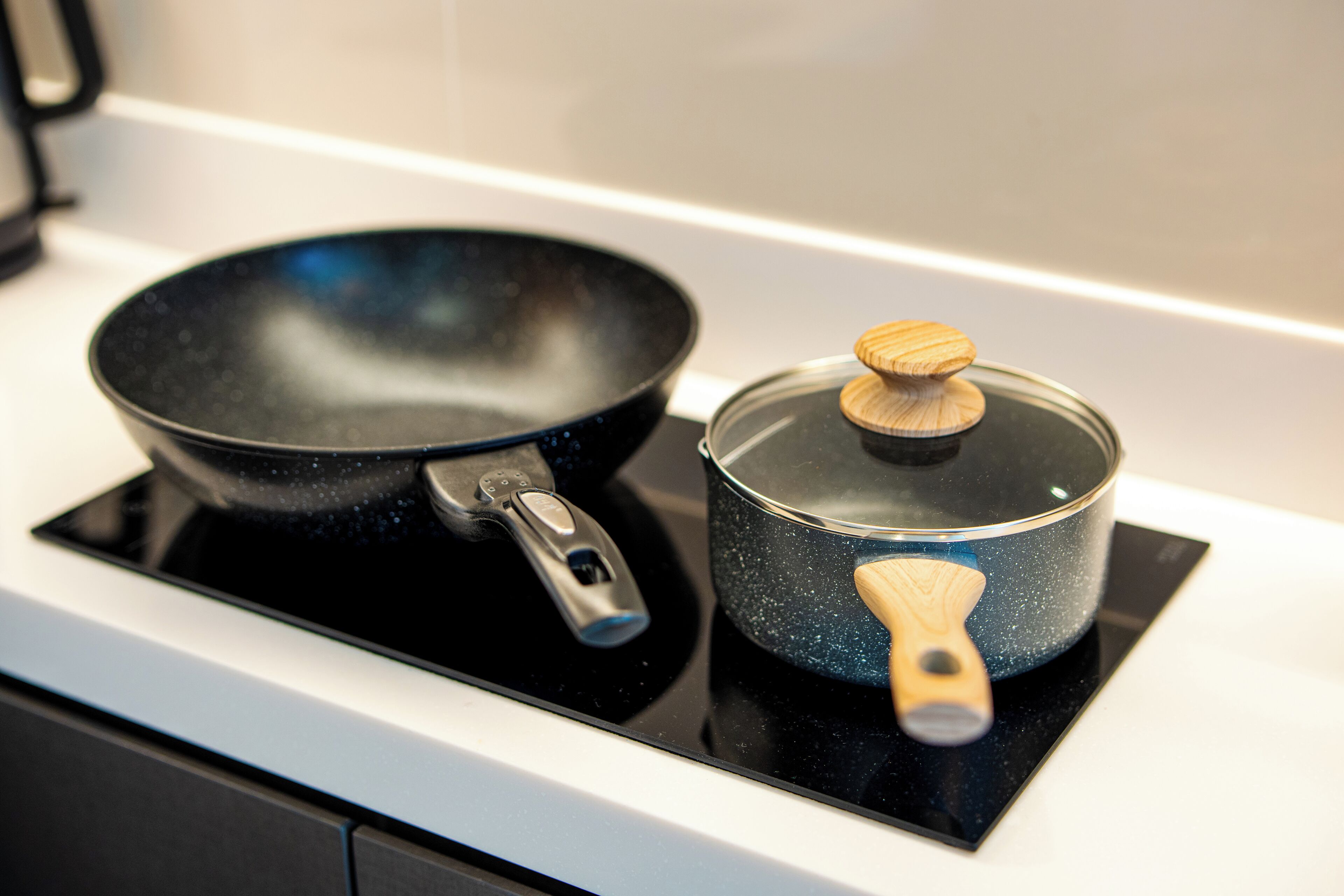 A kitchen with a black frying pan and a blue pot with a wooden handle on an induction cooktop.