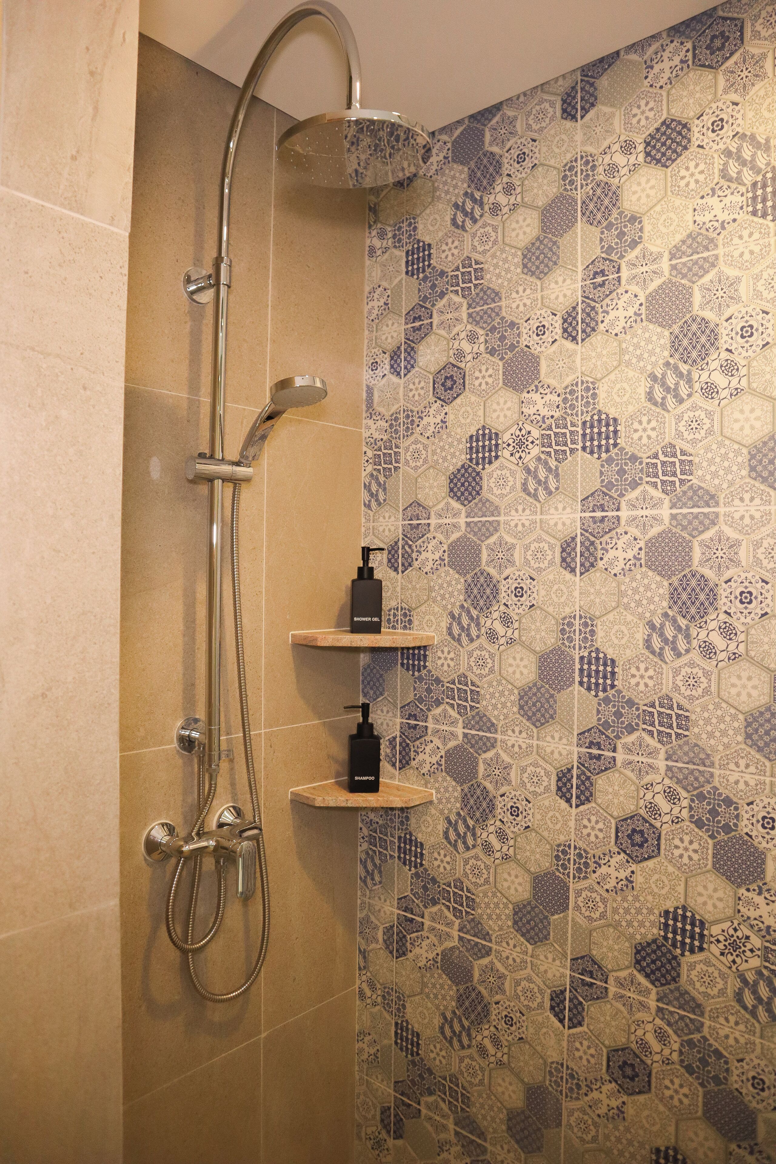 Eine Dusche mit Handbrause und Regendusche, ein Seifenspender sowie eine Shampoo-Flasche auf einem Regal.