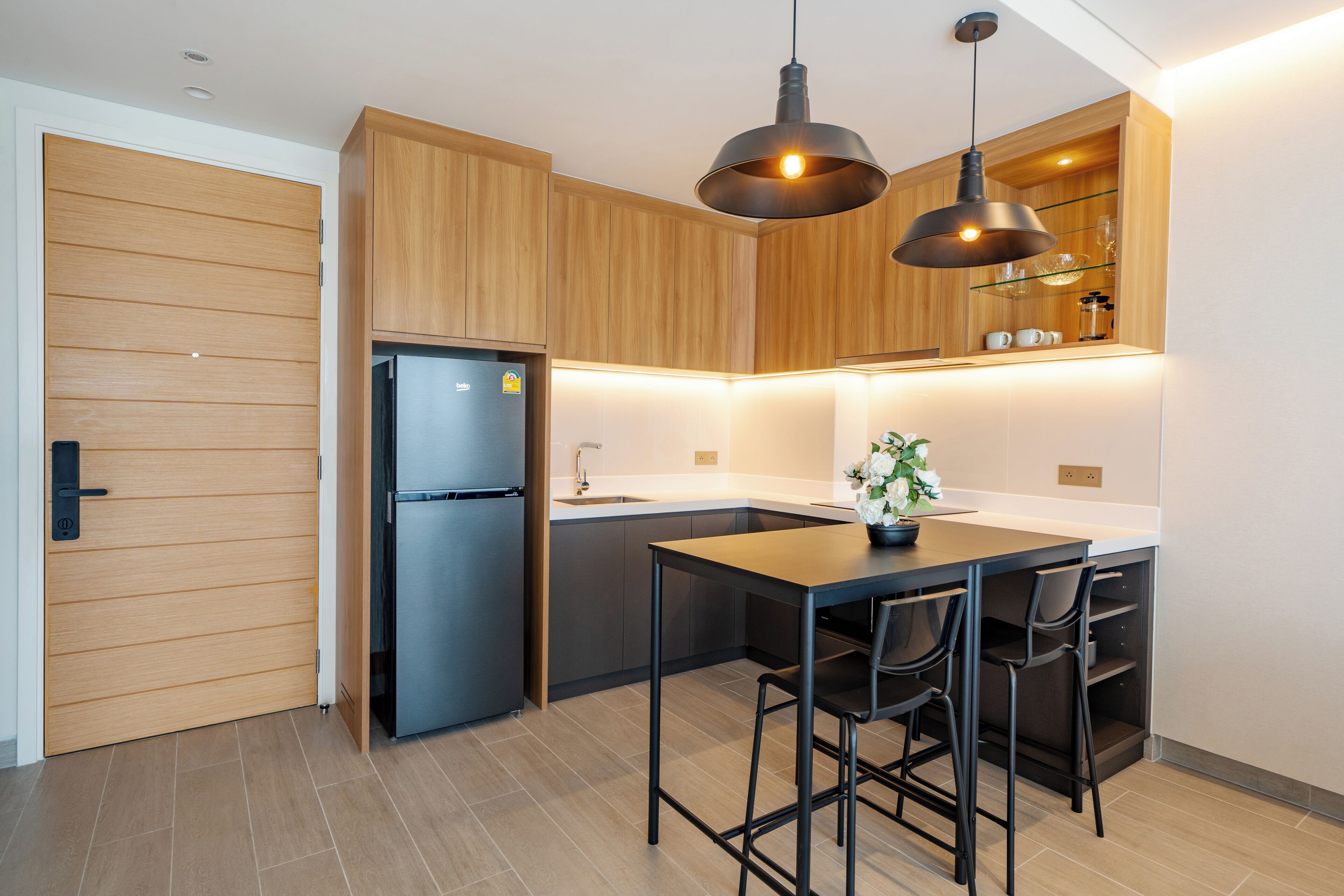 Een moderne keuken met houten kastjes, een zwarte koelkast, een eettafel met stoelen en hanglampen.