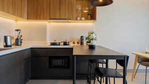 A modern kitchen with wooden cabinets, a built-in oven, a dining area with a table and chairs, and a pendant light.
