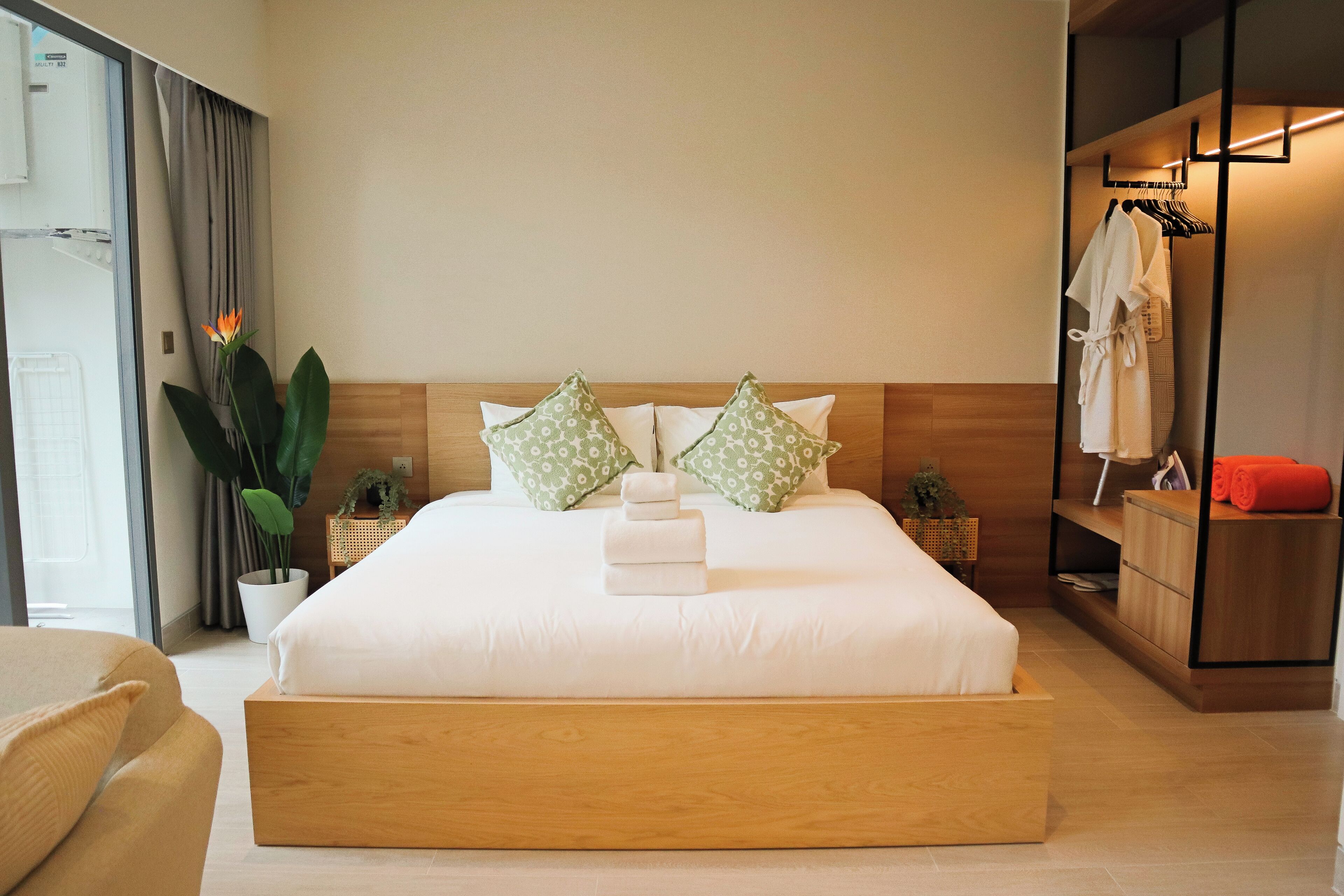 Ett modernt hotellrum med en stor säng, ett träbeklätt sänggavel och en garderob med upphängningsmöjligheter för kläder.