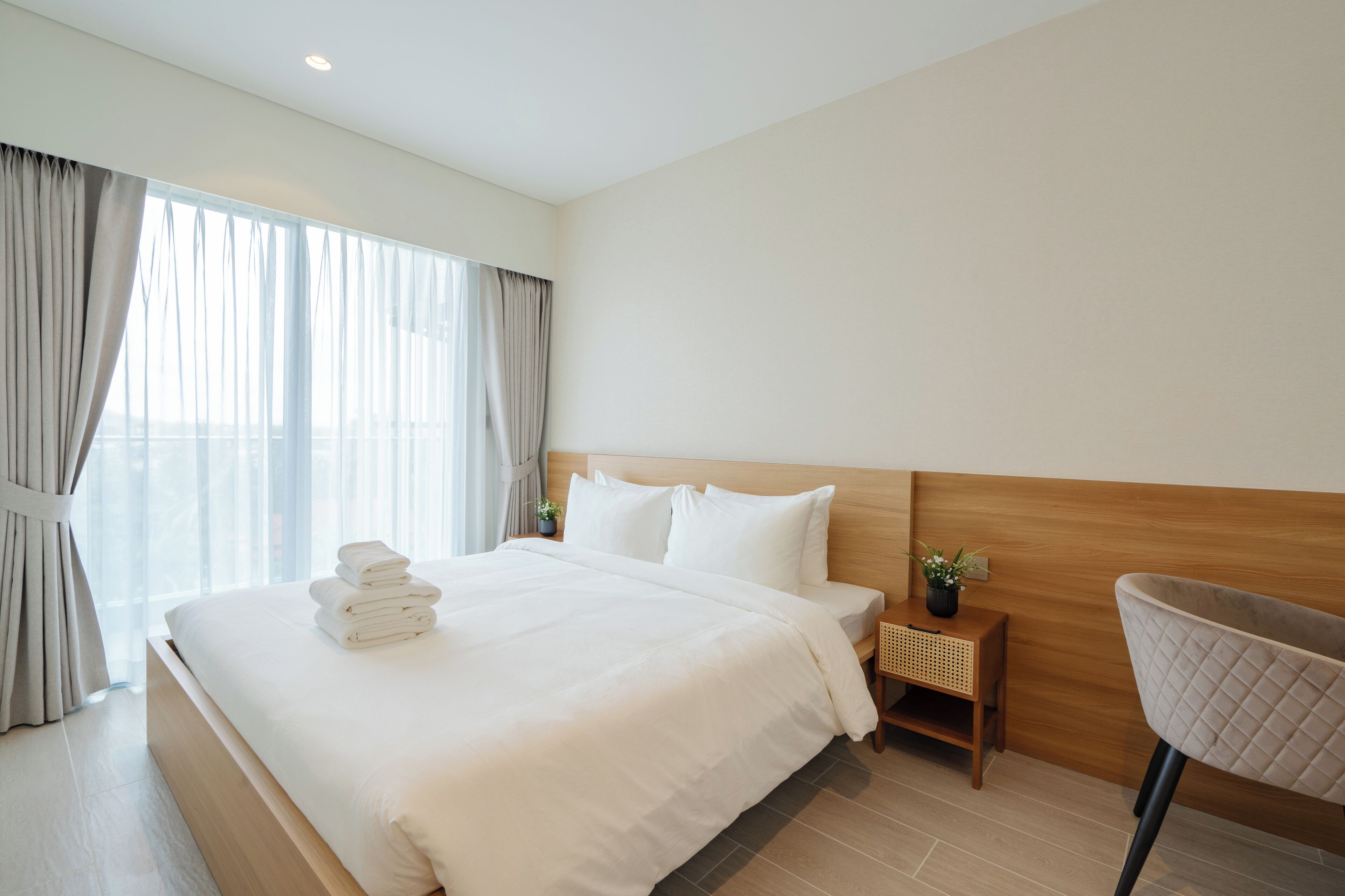 A hotel room with a large bed, a wooden headboard, a nightstand with a plant, and a chair.