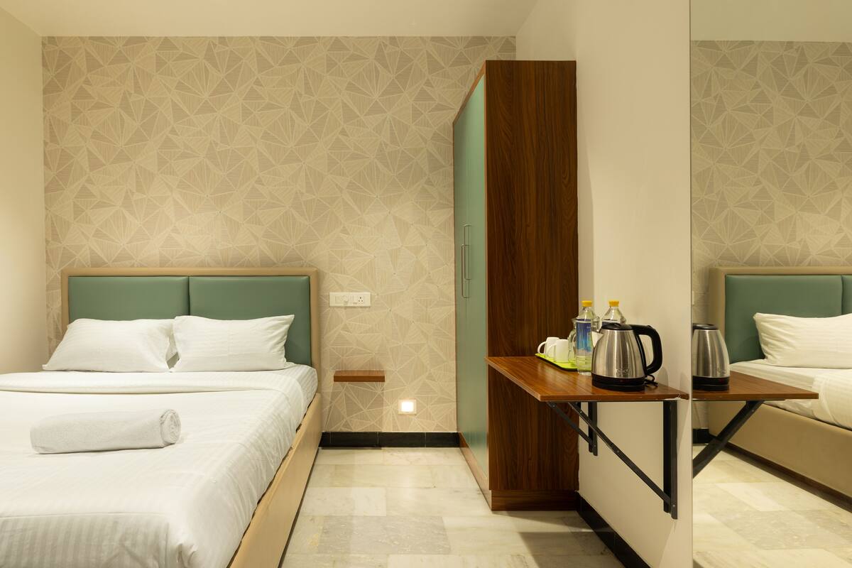 Habitación de hotel con dos camas, una mesita de madera con una tetera y botellas, y una pared con estampado geométrico.
