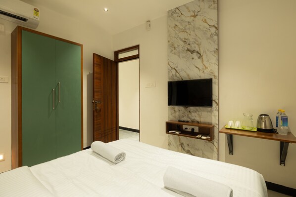 Une chambre d’hôtel comprenant un lit, une télévision, une armoire en bois, un mur en marbre et une petite étagère avec des articles de toilette.