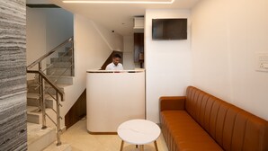 Un espace d’accueil comprenant un comptoir de réception, un escalier, un coin salon et un téléviseur fixé au mur.