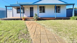 A single-story house with a blue roof and white walls, a front porch, and a paved driveway.