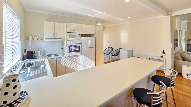A modern kitchen with white cabinets, a central island with bar stools, a microwave, oven, and a refrigerator.