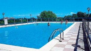 A swimming pool with clear blue water, a tiled deck, and a metal railing.