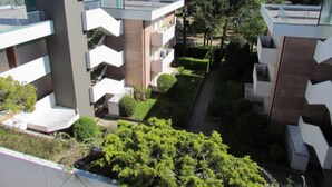 A multi-story residential building with balconies, a small garden area, and a view of the surrounding trees and sky.