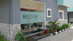A building with a glass facade and the name "BEDROCK RESIDENCES" visible. There are potted plants and a black and white curb in front.