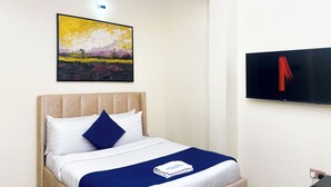 A neatly made bed with a blue and white bedspread, a single blue pillow, and a white pillow. A framed painting of a landscape hangs above the bed.