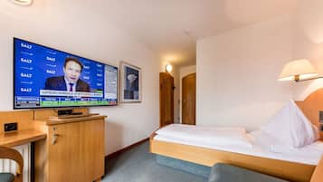 Habitación de hotel con cama, escritorio, televisión mostrando noticias financieras y un cuadro en la pared.