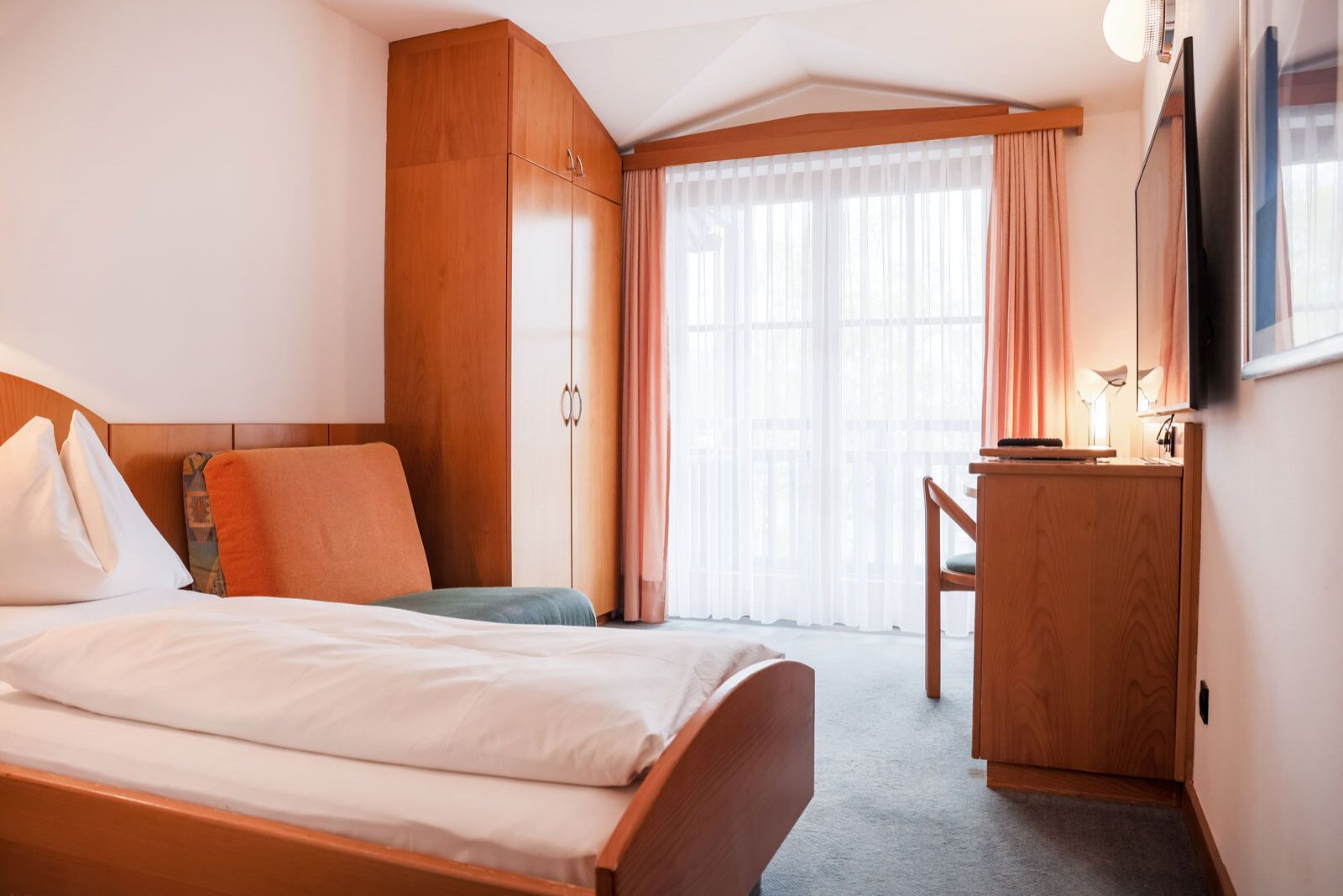 Una habitación de hotel con una cama, un armario de madera, un escritorio con silla y un televisor.