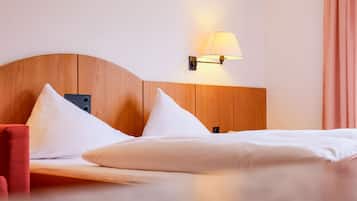 A hotel room with a wooden headboard, two white pillows, a red chair, and a wall-mounted lamp.