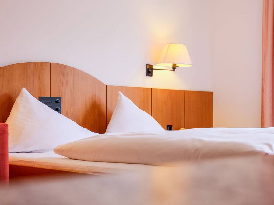 Ein Hotelzimmer mit einem hölzernen Kopfende, zwei weißen Kissen, einem roten Sessel und einer Wandleuchte.