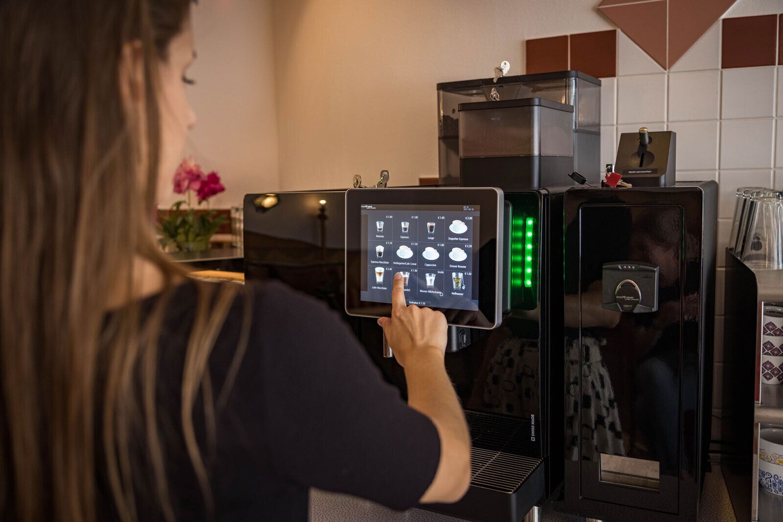 A person interacting with a coffee machine, selecting a beverage from a touchscreen menu.