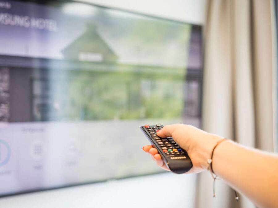 Una mano sosteniendo un control remoto frente a una pantalla de televisión que muestra Samsung Hotel.