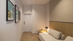 A modern hotel room with a wooden floor, a sofa, a nightstand with a lamp, and framed pictures on the wall. - Rubio Rooms by Concept Flats (València)