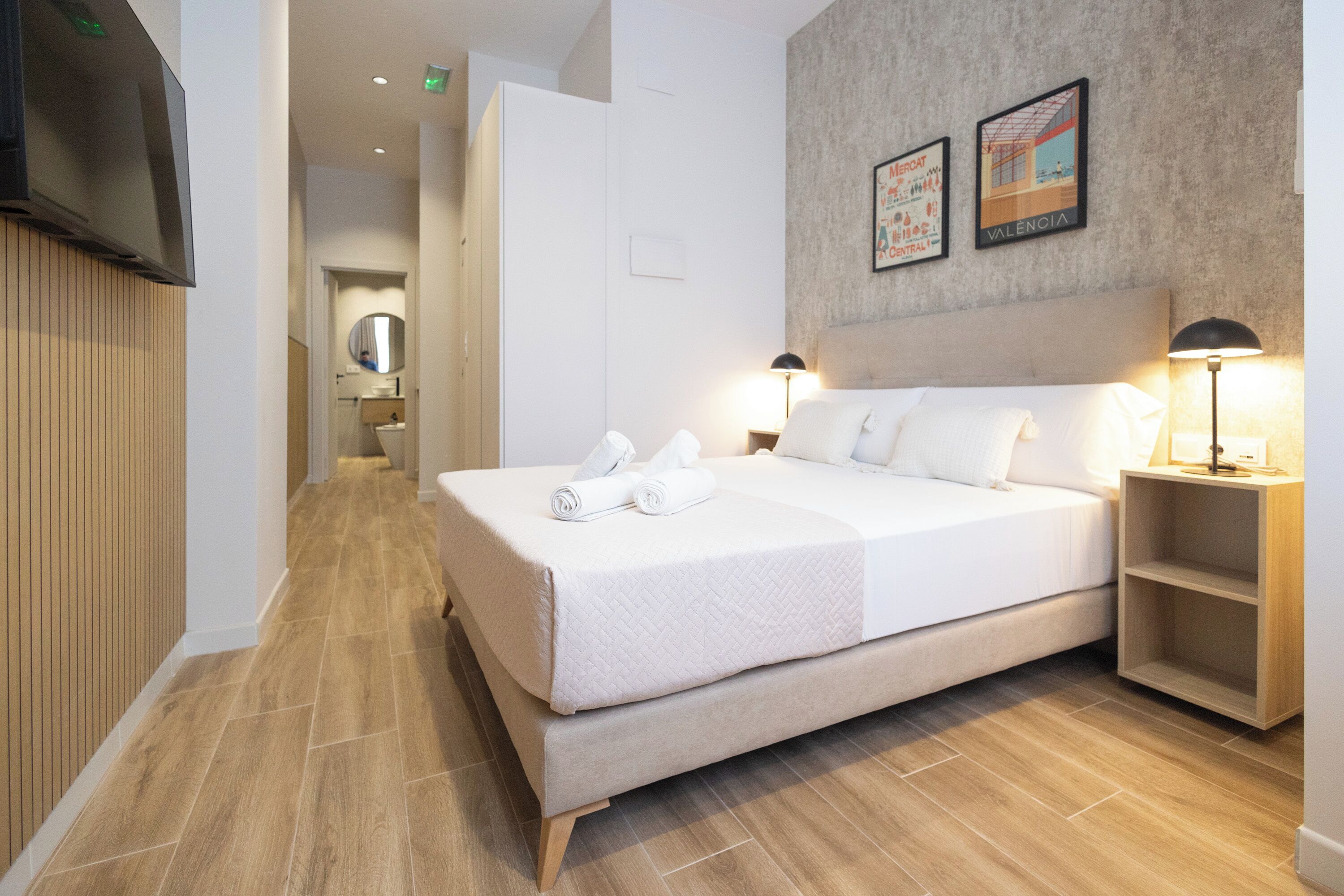 Una habitación de hotel moderna con una cama grande, lámparas de noche, un televisor de pantalla plana y suelo de madera.