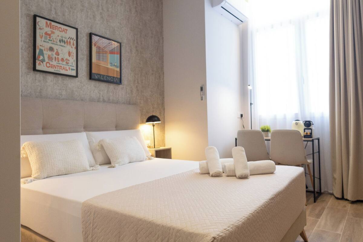 A hotel room with a large bed, a desk, and a chair. There are two framed pictures on the wall.
