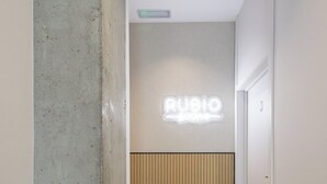 A hallway with a wooden floor, a concrete wall, and a wooden panel wall with a 'RUBIO' sign. - Rubio Rooms by Concept Flats (València)