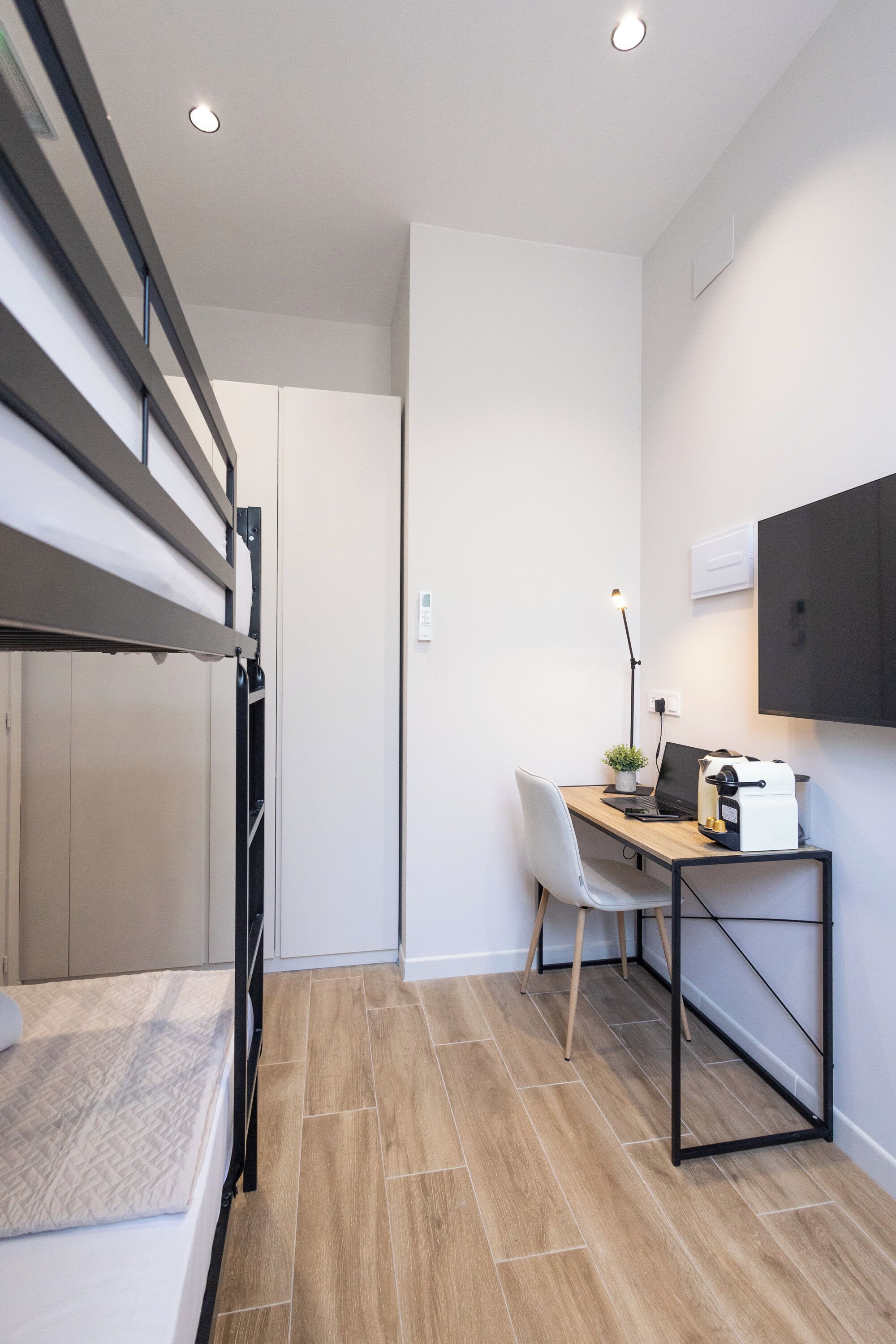 Habitación compacta con una litera, un escritorio con una computadora portátil, una silla y una pequeña planta.