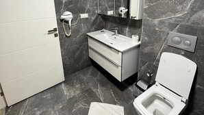 A modern bathroom with a marble floor, a white vanity with a mirror, a toilet, and a hairdryer on the wall. - EF SUİT OTEL (Ankara)