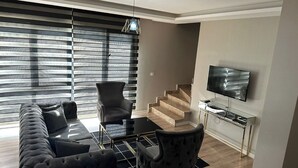 A modern living room with a sofa, armchairs, a coffee table, a TV, and a staircase. - EF SUİT OTEL (Ankara)