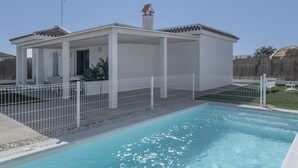 A poolside house with a covered patio, a fenced swimming pool, and a clear sky.