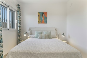 A bedroom with a bed, two bedside lamps, a painting on the wall, and a window with curtains.
