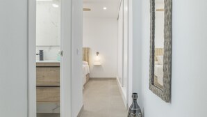 A hallway with a mirror, a vase, and a bed with a nightstand.