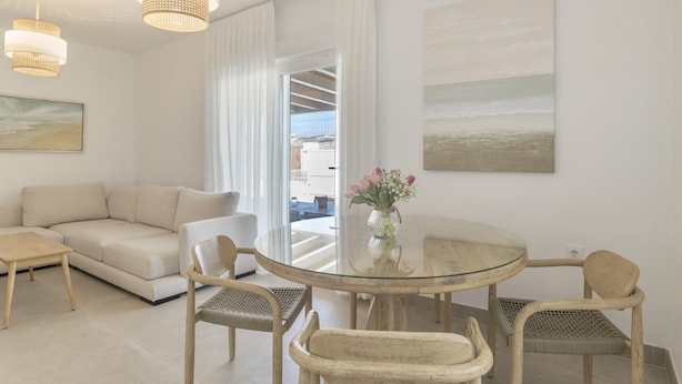 A modern living room with a glass dining table, wicker chairs, a sofa, and a painting on the wall.