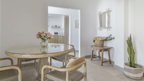 A dining area with a glass table, wicker chairs, a vase with flowers, a wooden side table, and a potted plant.