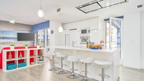 A modern kitchen with white cabinets, a central island with bar stools, and a large window overlooking a beach. - Apartment 'Penthouse with Terrace and Private Jacuzzi' with Sea View, Wi-Fi and Air Conditioning (Almuñécar)