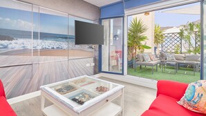 A modern living room with a large glass wall, a flat-screen TV, and a glass coffee table with decorative items. - Apartment 'Penthouse with Terrace and Private Jacuzzi' with Sea View, Wi-Fi and Air Conditioning (Almuñécar)