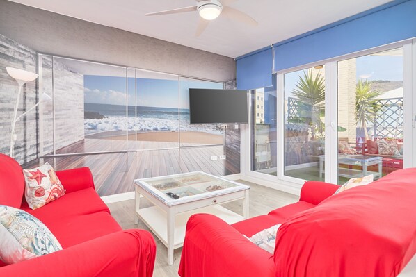 A modern living room with a large glass wall, red furniture, and a ceiling fan.
