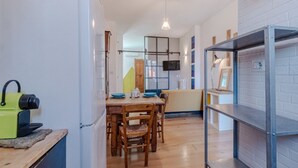 A compact kitchen with a dining area, a TV mounted on the wall, and a shelf unit. - GuestHost - Bright Apartment Lingotto Torino (Turin)