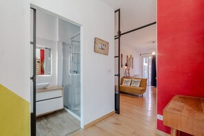 A modern interior with a glass shower, a white sink, a wooden cabinet, a sofa, and a red accent wall.