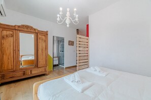 A bedroom with a bed, a wooden wardrobe, a mirror, a chandelier, and a red accent wall.