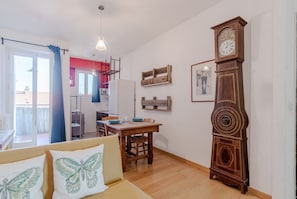 Une pièce comprenant une table à manger en bois, un canapé agrémenté de coussins à motifs papillons, une grande horloge en bois et un mur d’accent de couleur rouge.