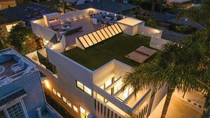 A modern house with a rooftop deck, a swimming pool, and a well-lit patio area.