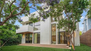A modern two-story house with large glass windows, a well-maintained lawn, and a tree with purple flowers.