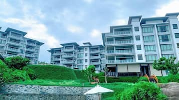 A modern hotel with multiple balconies, a swimming pool, and lush greenery.