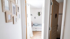 A hallway with wooden flooring, white walls, and a bed with a blue blanket in the background.