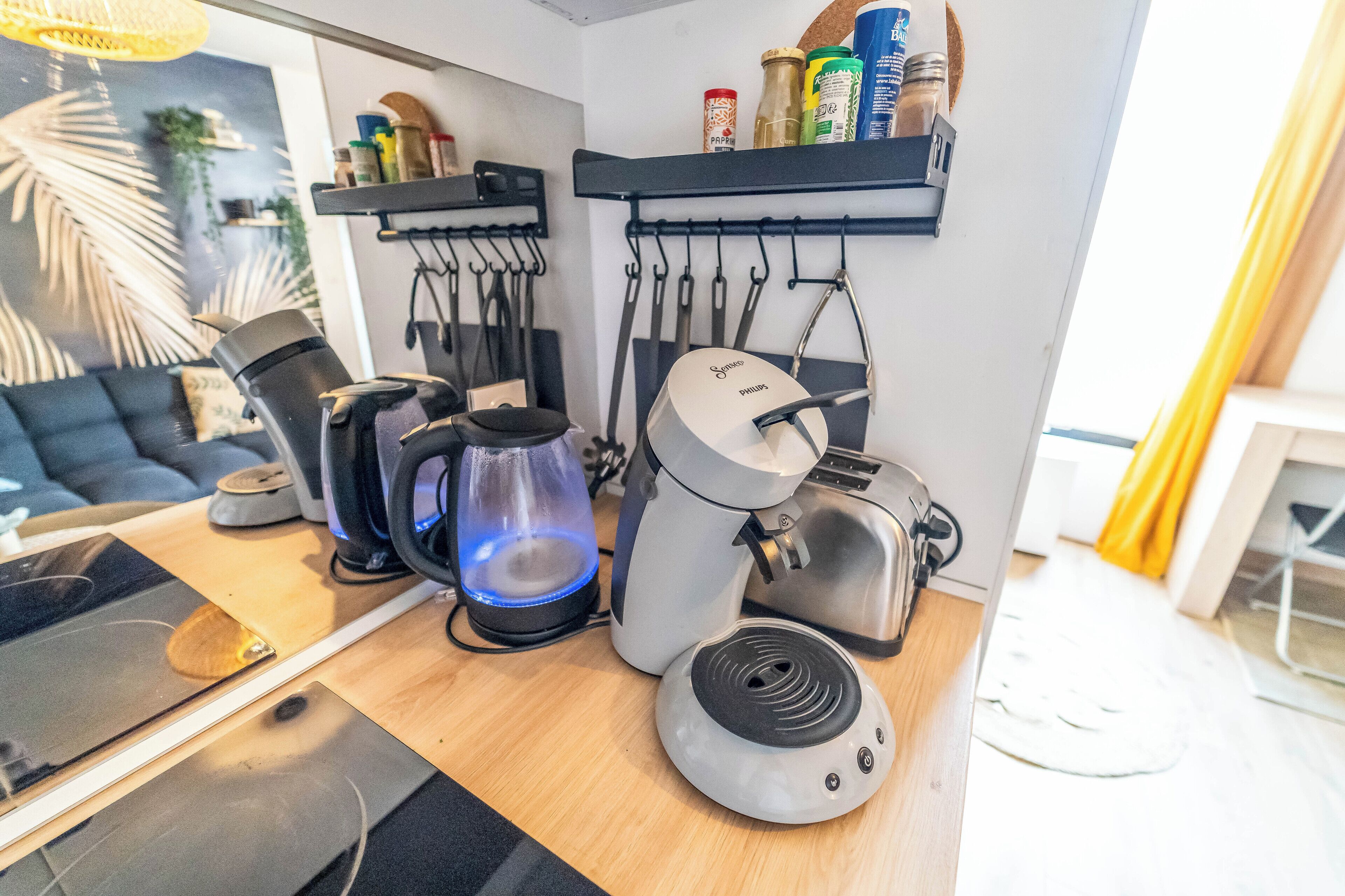 A kitchen with a coffee maker, toaster, and kettle on the counter. There are shelves above holding various kitchen items.