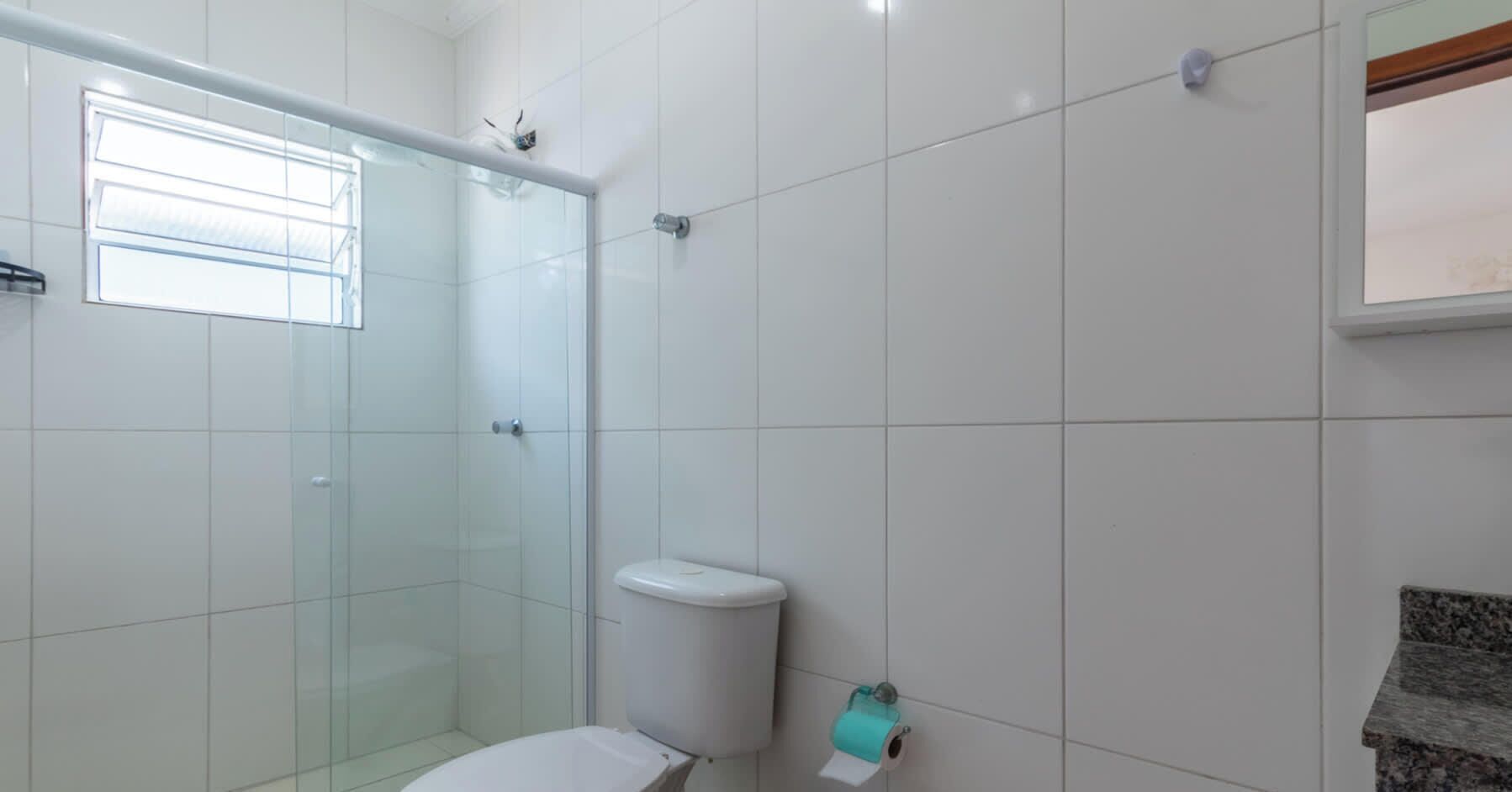 Une salle de bain avec des carreaux blancs, une douche en verre, des toilettes et une fenêtre.